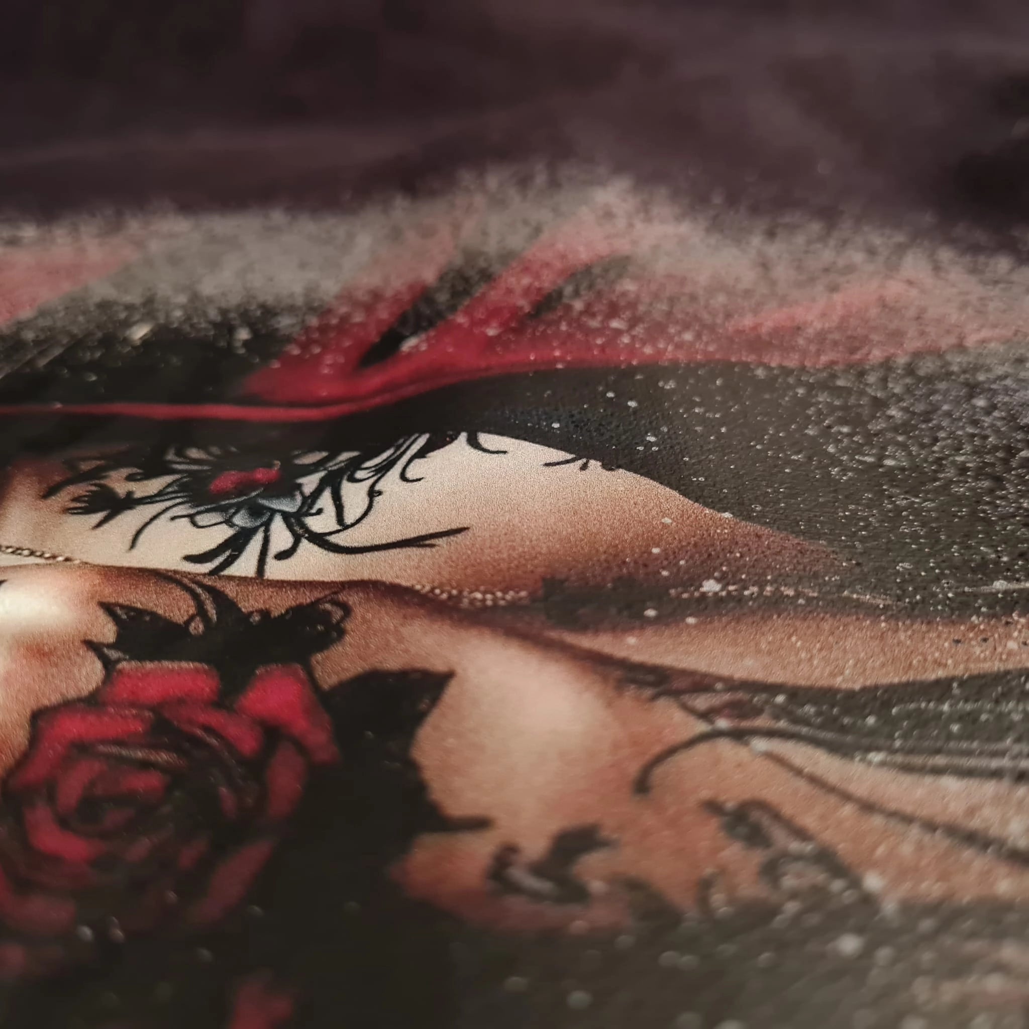 Close-up of a person with tattoos on their arm, including a red rose and black floral design.