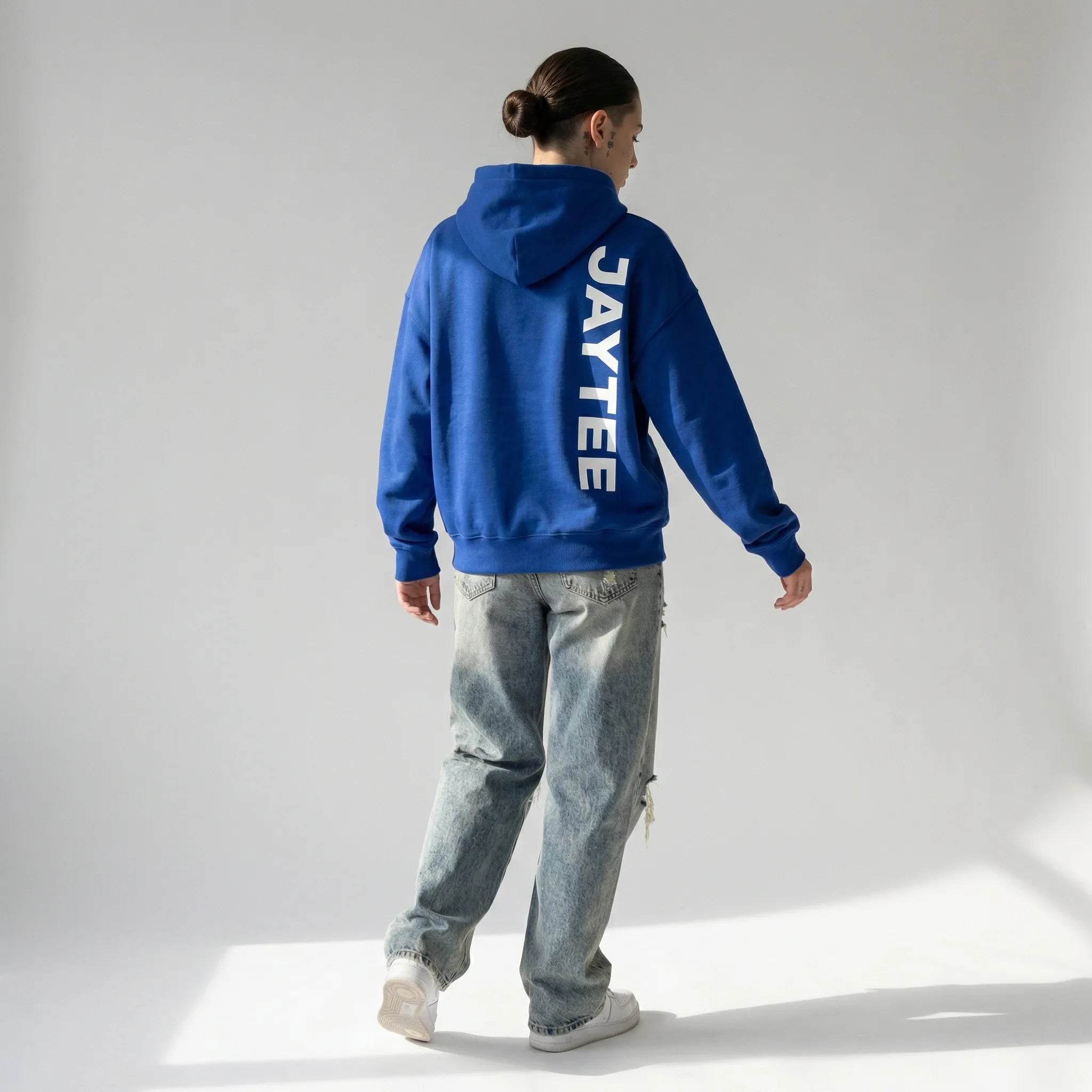 Person wearing a blue hoodie with 'JAYTEE' branding, standing on a light gray background