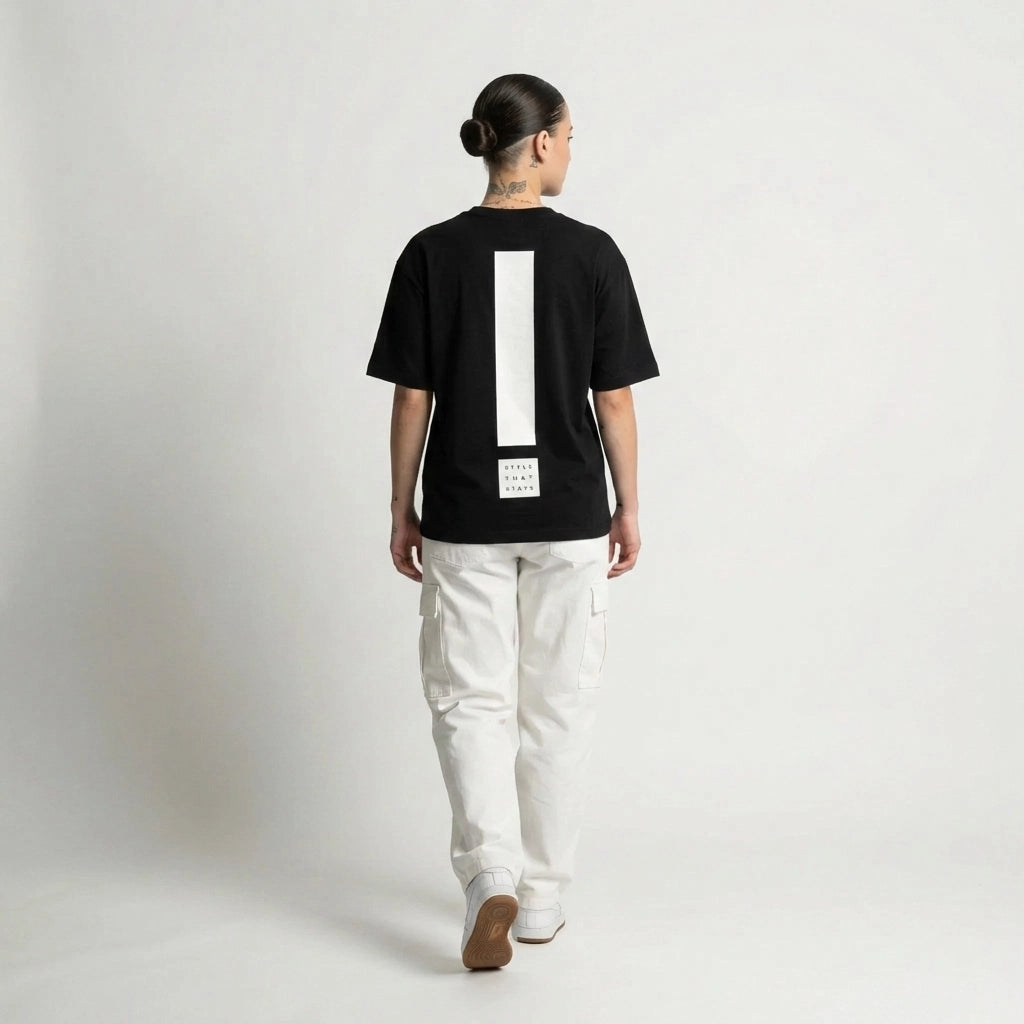 Person wearing a black JAYTEE t-shirt with a large white exclamation mark on the back, standing against a plain background.