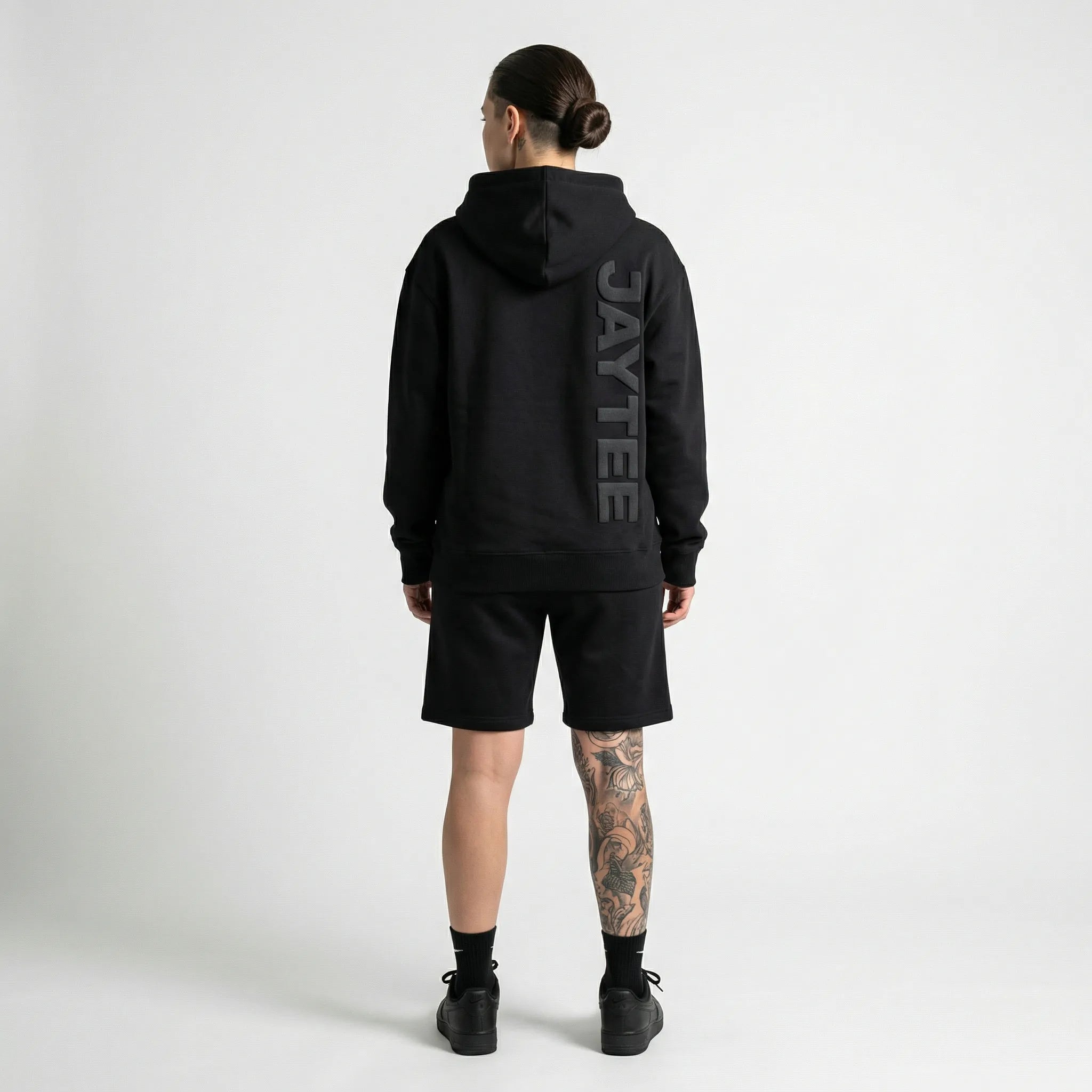 Person wearing a black hoodie with 'AYTEE branding on the back, standing against a white background.