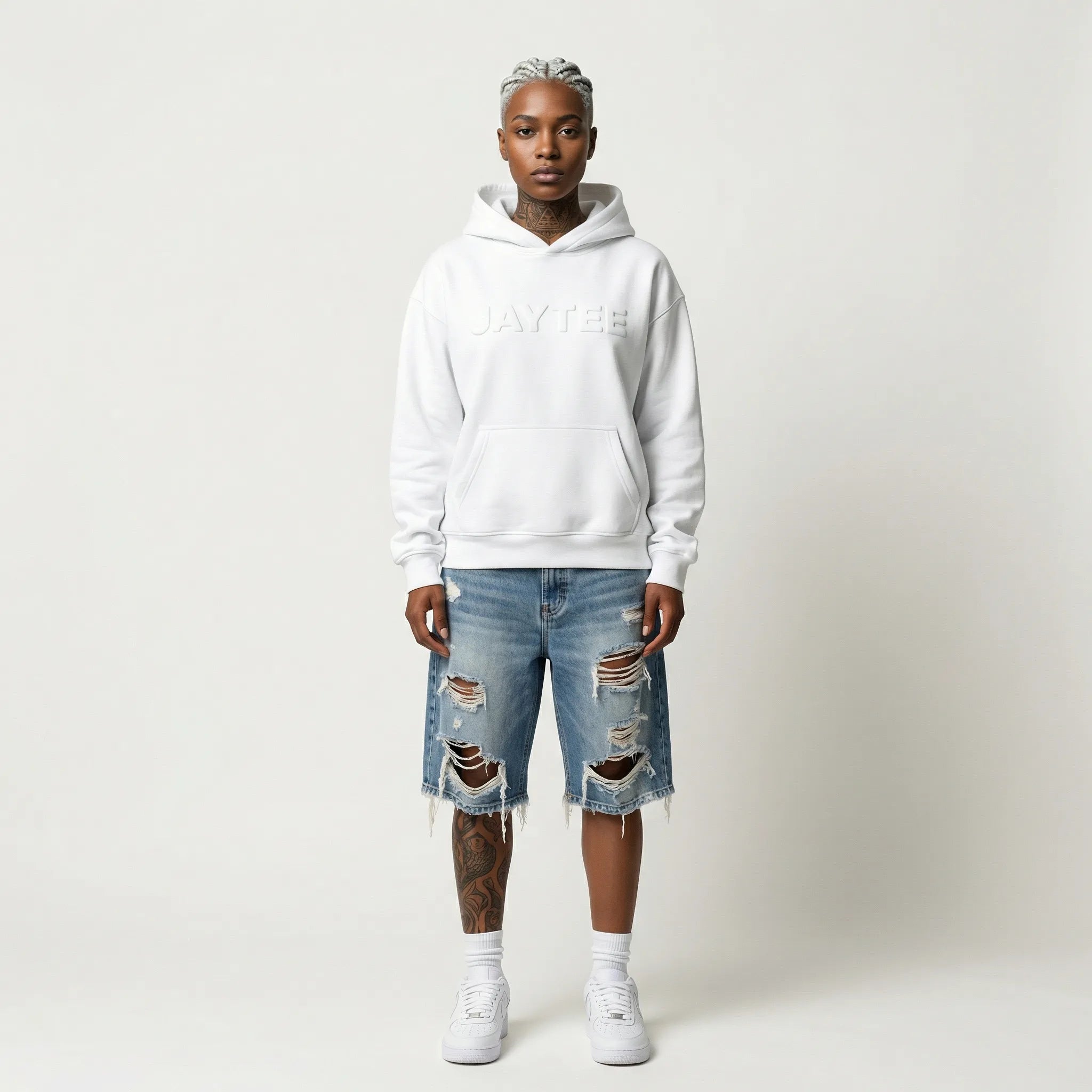 Person wearing a white JAYTEE hoodie and ripped jeans on a plain background