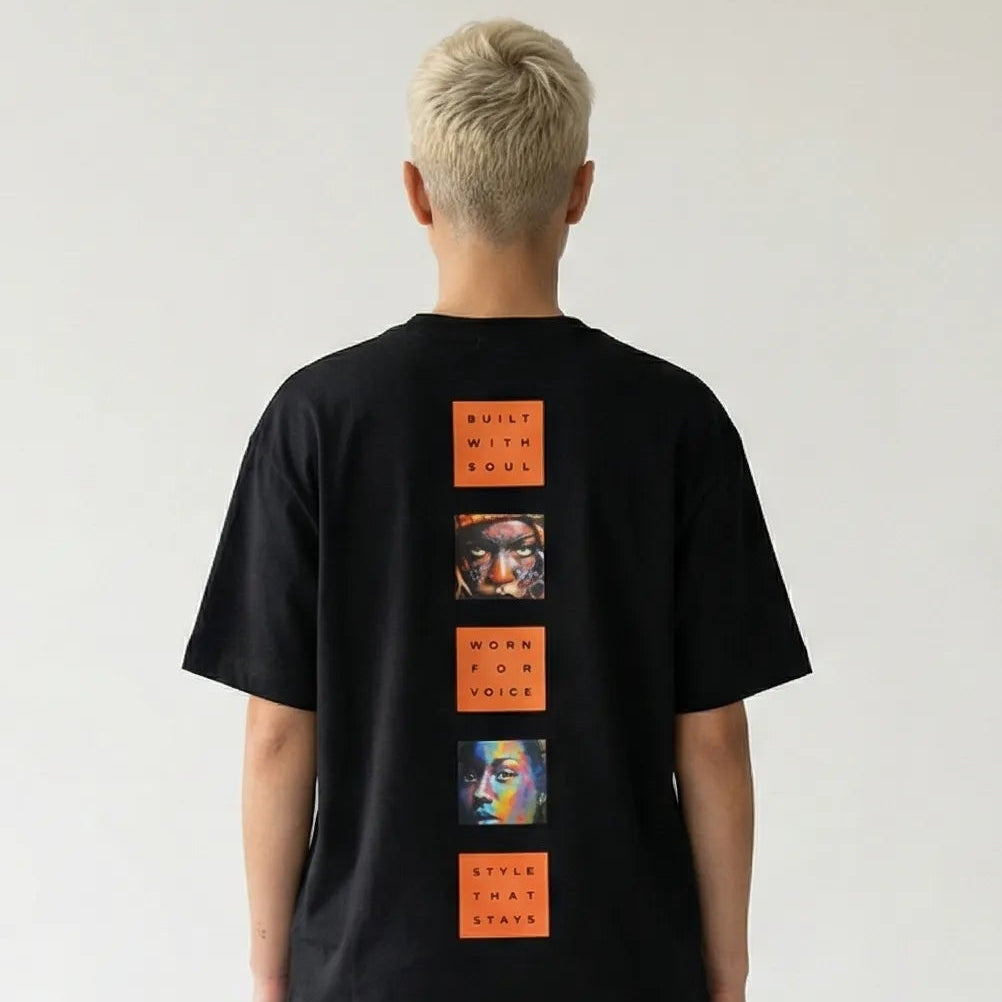 Person wearing a black JAYTEE t-shirt with orange graphic designs on the back, standing against a plain white background.