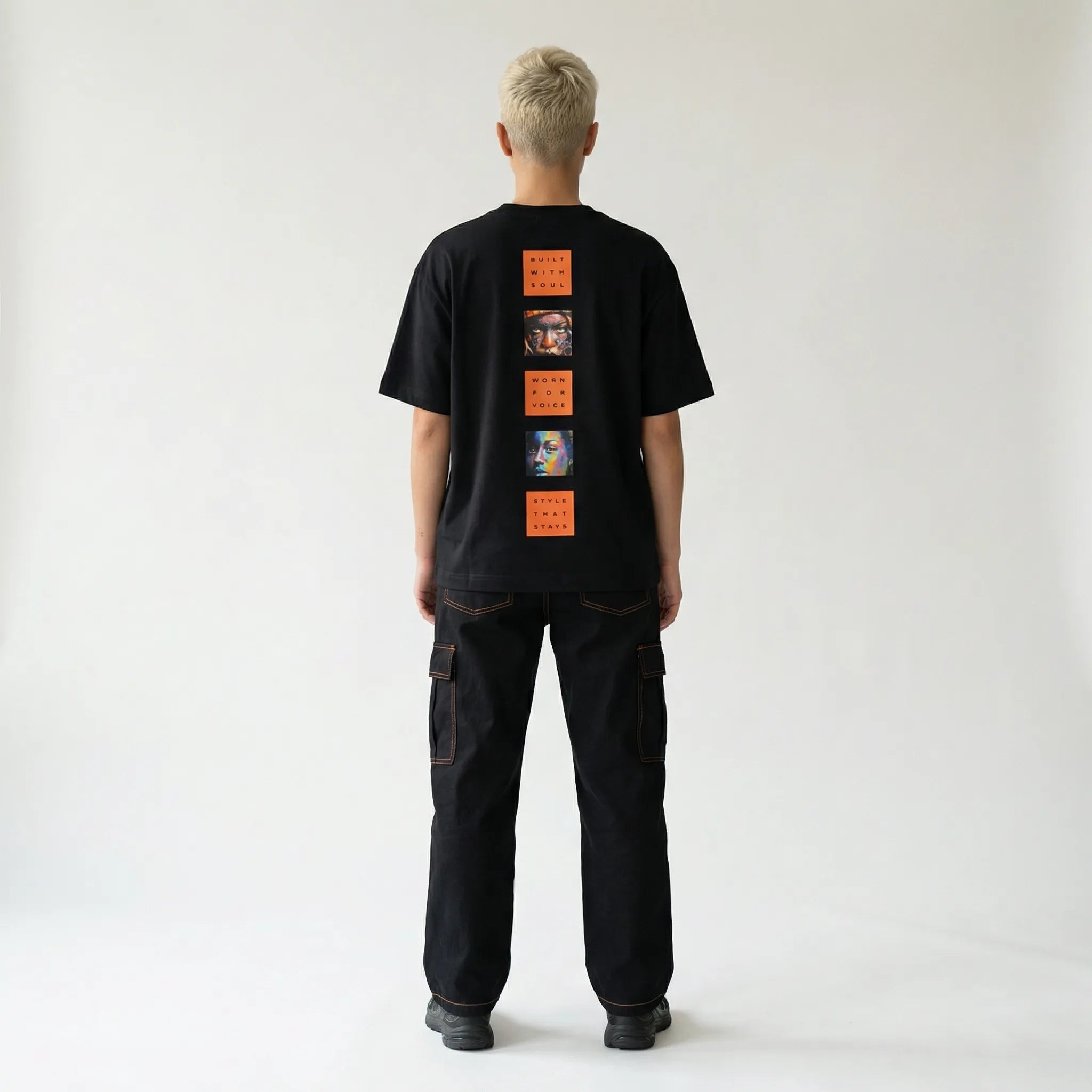 Person wearing a black JAYTEE t-shirt with orange graphic designs on the back, standing against a plain white background.
