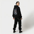Person wearing a black hoodie with a graphic design on the back against a white background