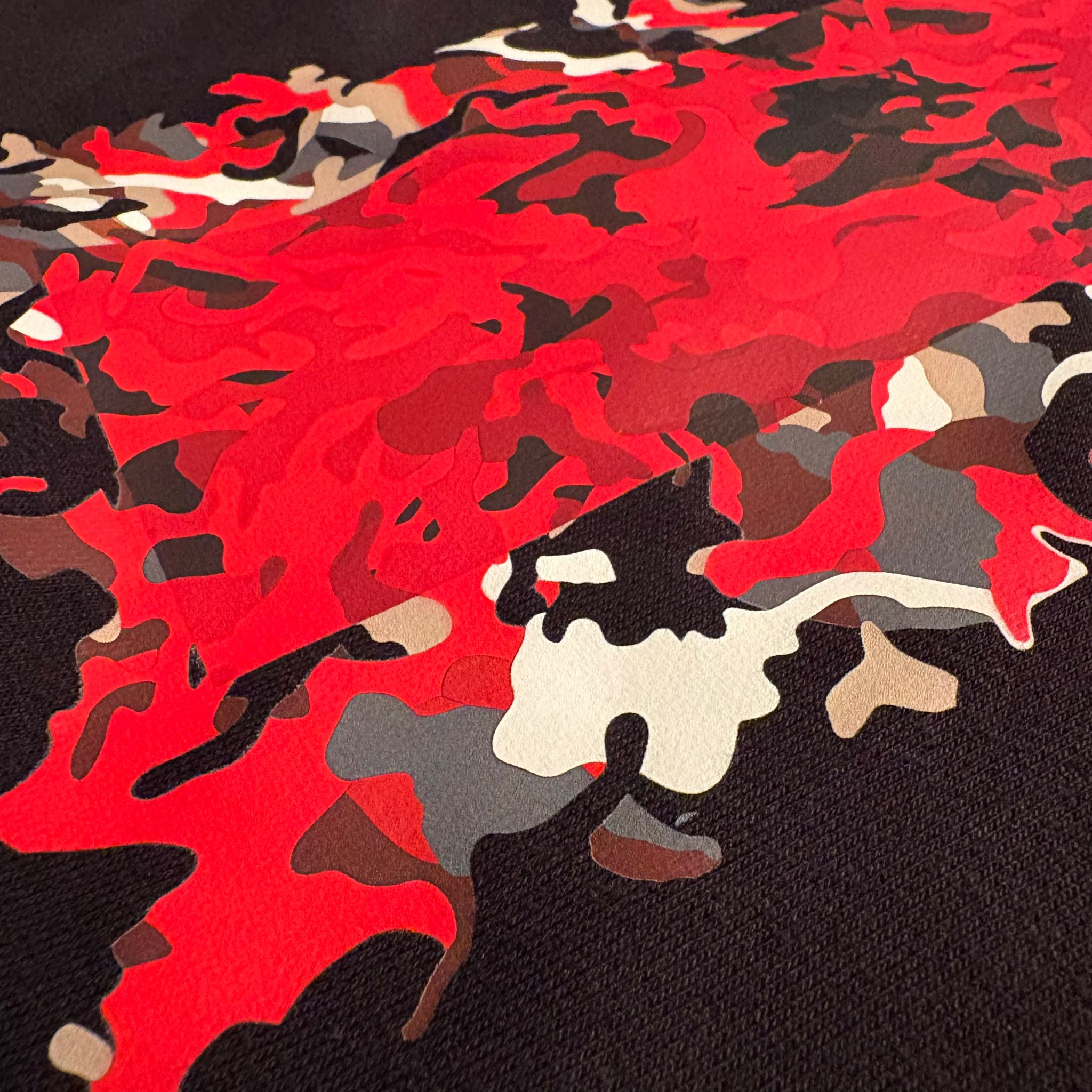 Camouflage pattern with red, black, gray, and beige colors on a textured surface.