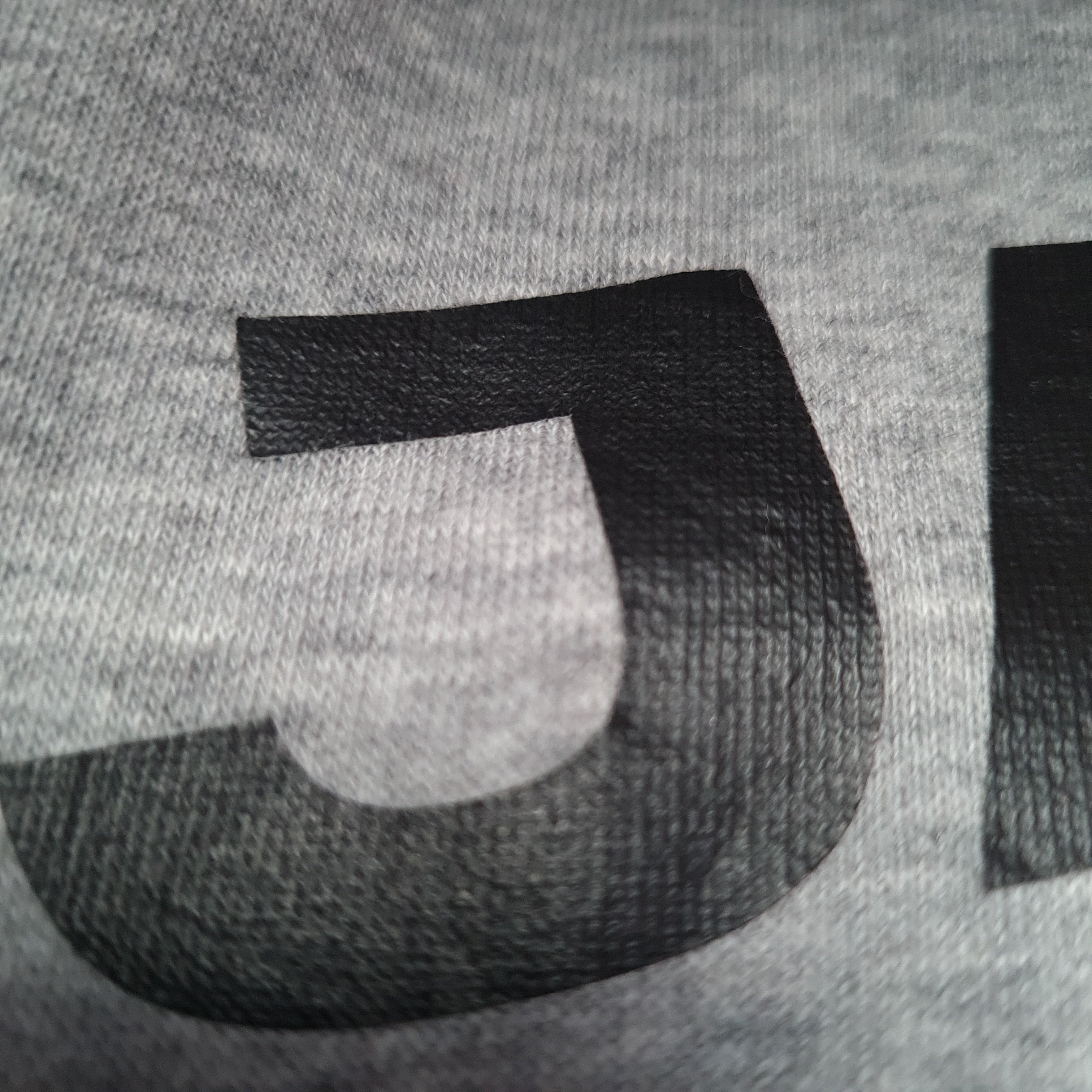 Close-up of a textured gray fabric with a black letter 'P' on a gray background