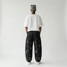 Person wearing black pants with white patterns on a plain background, view from back