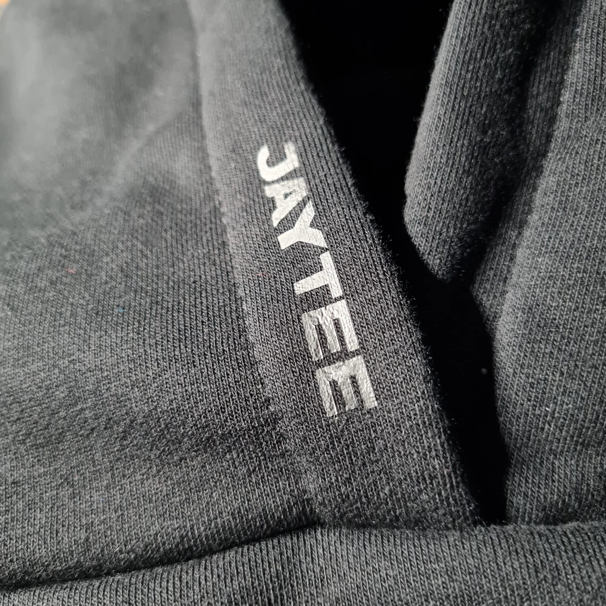 Close-up of a black hoodie with 'JAYTEE' branding.