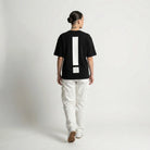 Person wearing a black JAYTEE t-shirt with a large white exclamation mark on the back, standing against a plain background.