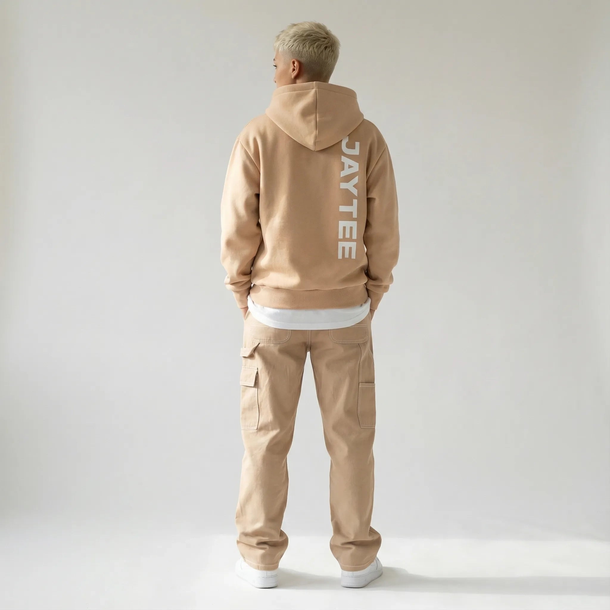 Person wearing a sand hoodie and pants with JAYTEE branding on a plain background