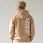 Person wearing a sand JAYTEE hoodie and pants on a plain background