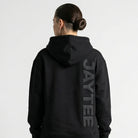 Person wearing a black hoodie with 'AYTEE branding on the back, standing against a white background.