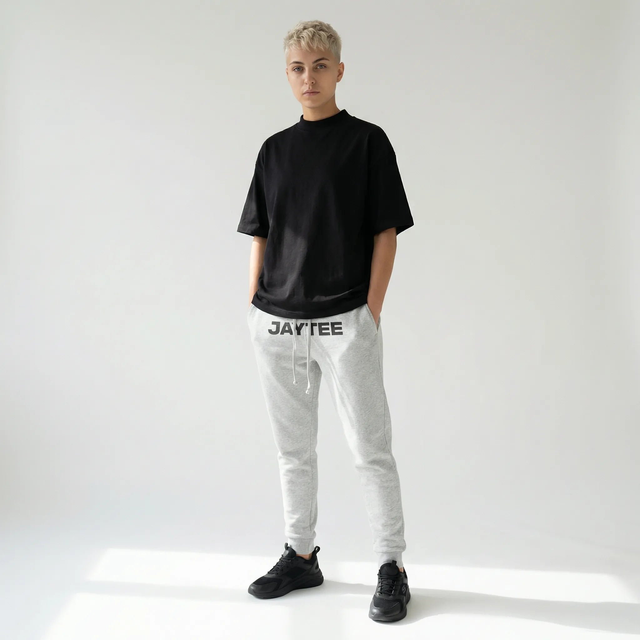 Person wearing a black t-shirt and gray sweatpants with JAYTEE branding on a white background