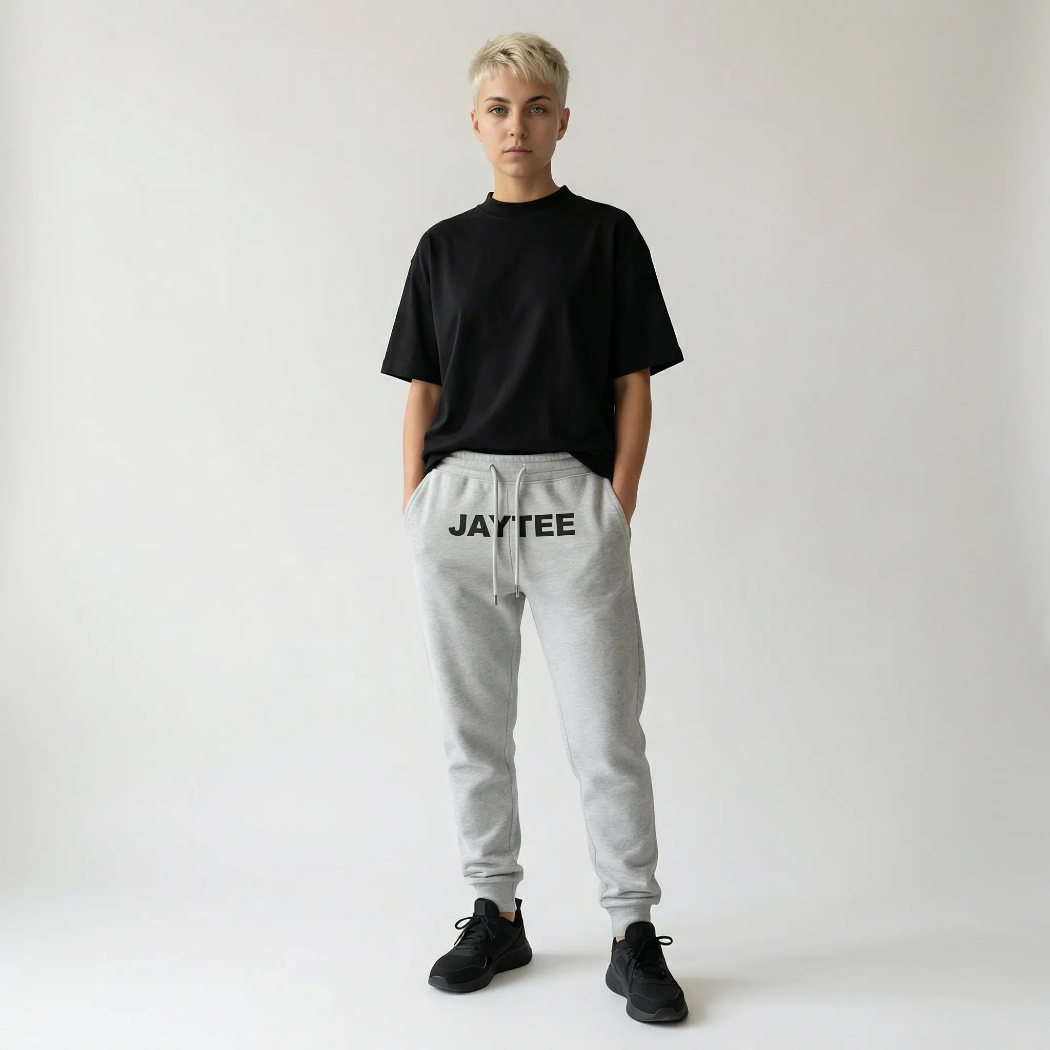 Person wearing a black oversized t-shirt and gray sweatpants with JAYTEE branding on a white background