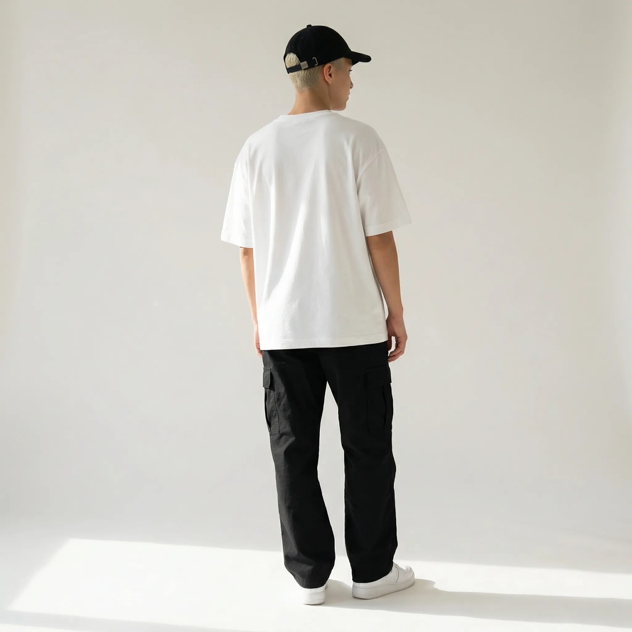 Person wearing a white JAYTEE t-shirt, black pants, and a black cap on a plain background