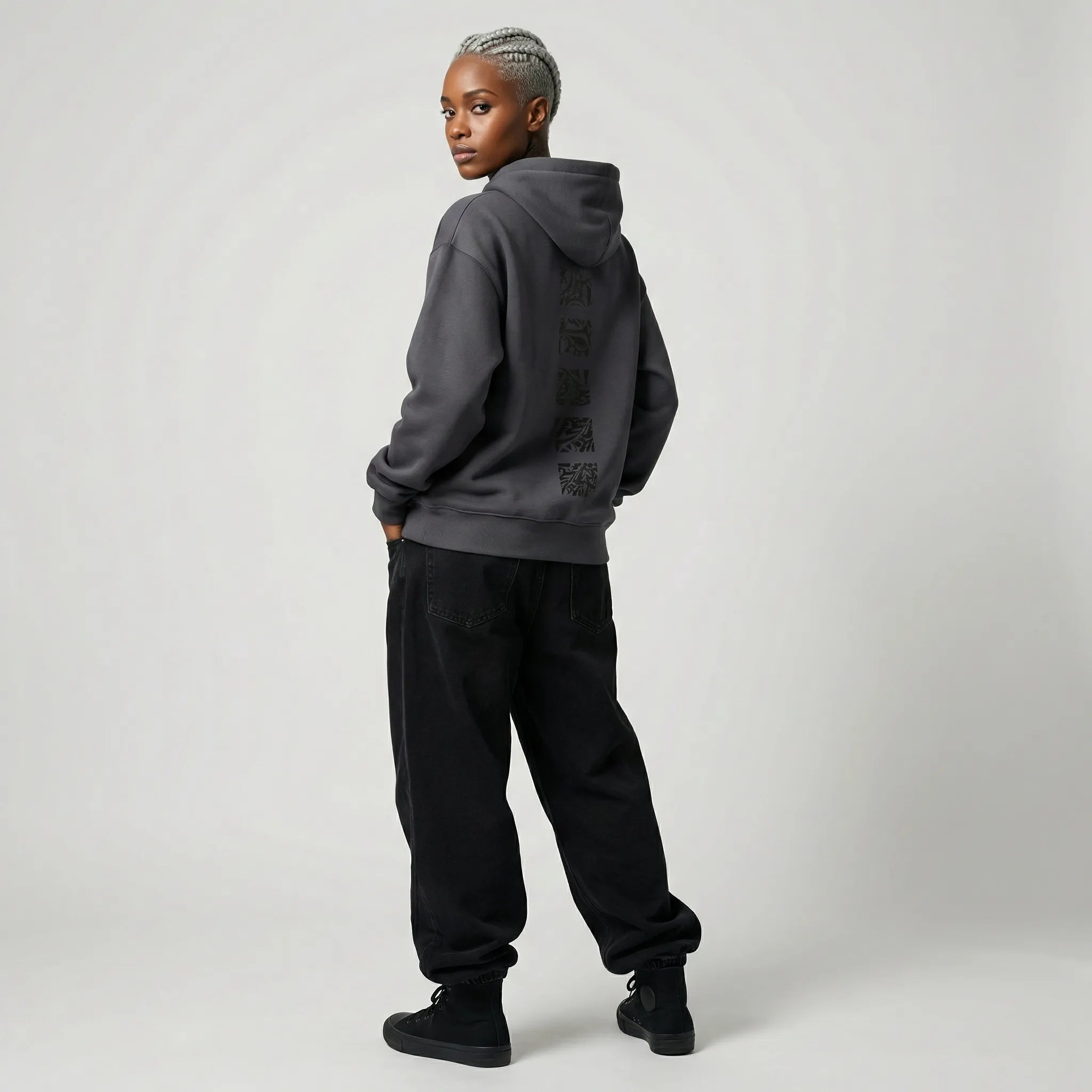 Person wearing a dark gray  JAYTEE hoodie and black pants on a light gray background