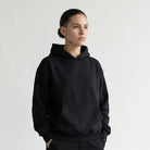 Person wearing a black JAYTEE hoodie and black pants on a white background