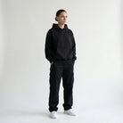 Person wearing a black JAYTEE hoodie and black pants on a white background