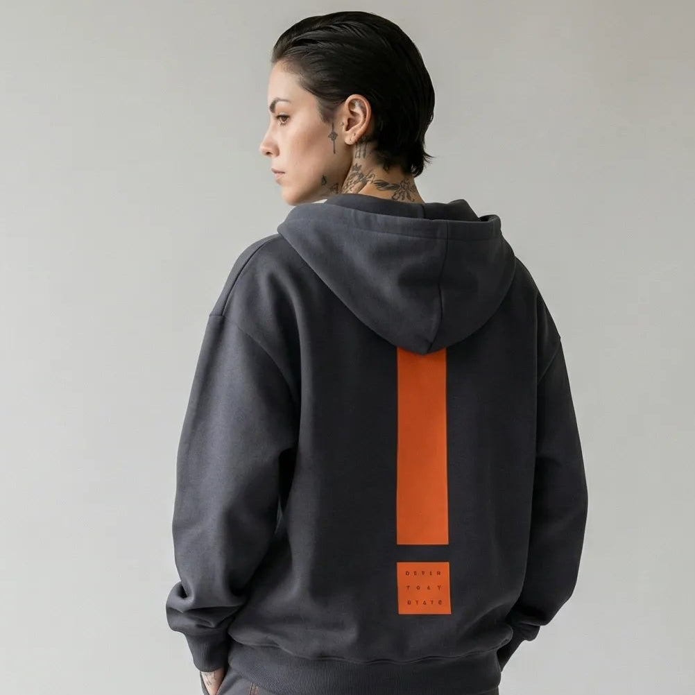 Person wearing a dark gray  JAYTEE hoodie and pants with an orange exclamation mark on the back, standing against a plain background.