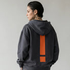 Person wearing a dark gray  JAYTEE hoodie and pants with an orange exclamation mark on the back, standing against a plain background.