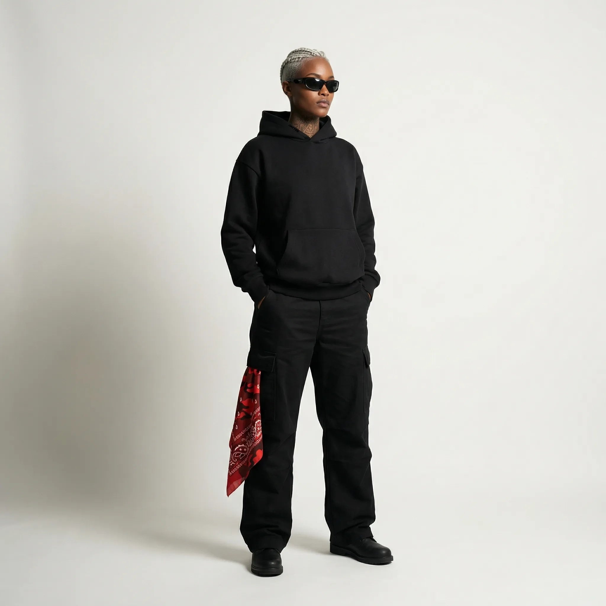 Person wearing a black  JAYTEE hoodie and pants with a red bandana, standing against a plain background