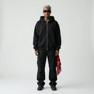 Person wearing a black  JAYTEE hoodie and pants holding a red and black patterned bandana on a white background