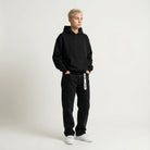 Person wearing a black JAYTEE hoodie and black pants with white text on a white background