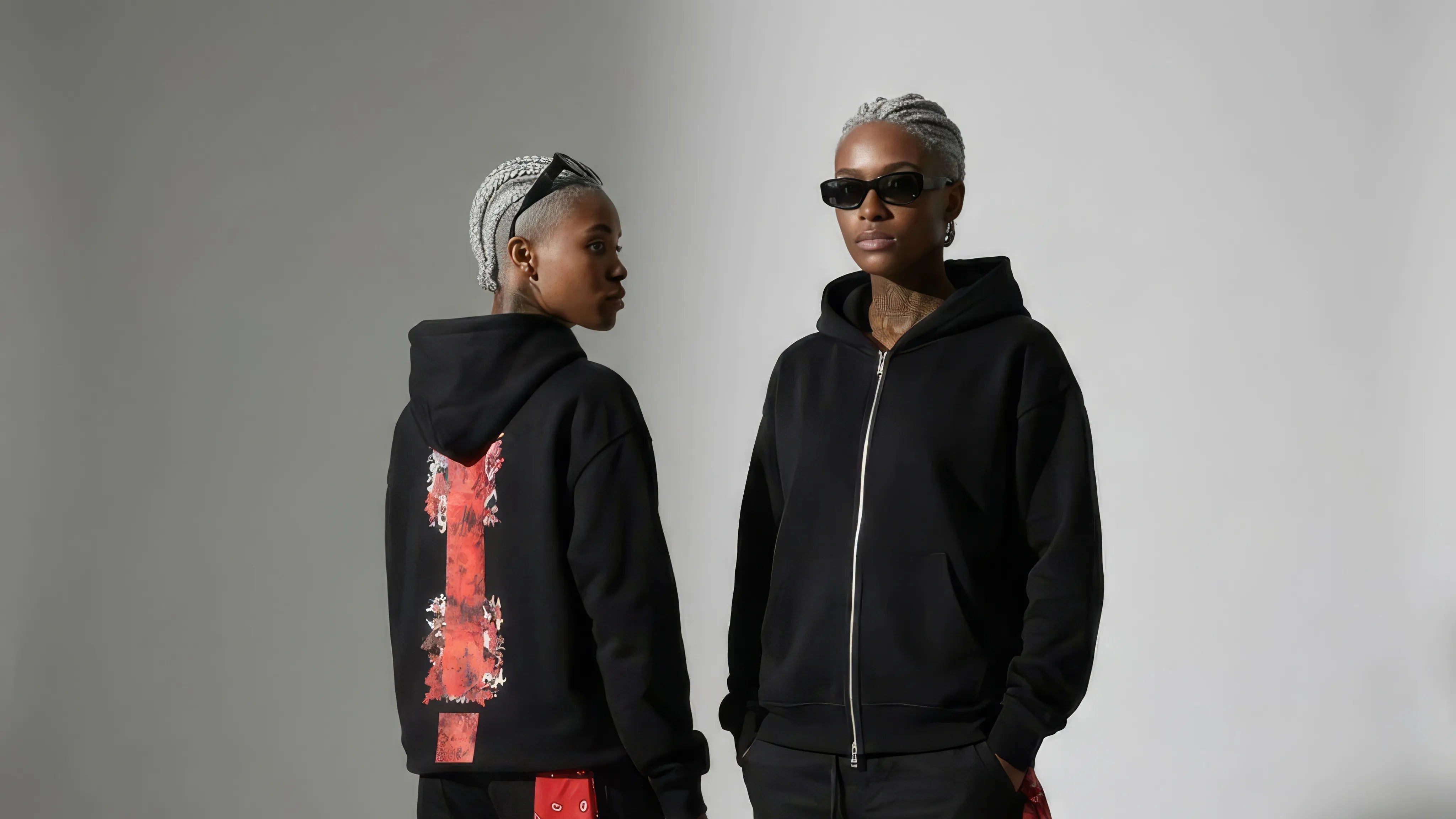 Two people wearing black hoodies with unique designs on a gray background