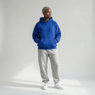 Person wearing a blue JAYTEE hoodie and gray sweatpants on a white background