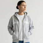 Person wearing a gray hoodie with 'JAYTEE' branding, white t-shirt, blue jeans, and white sneakers on a light gray background.