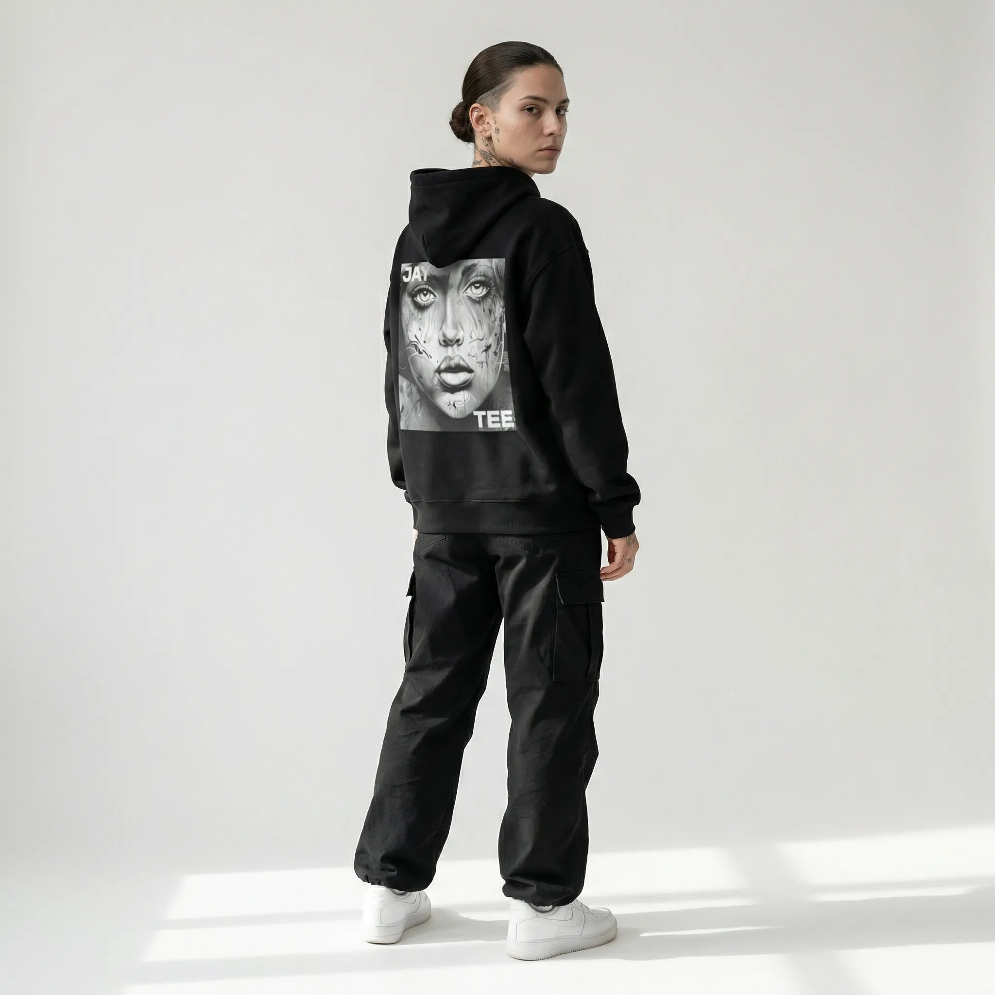 Person wearing a black JAYTEE hoodie with a graphic design on the back, standing against a white background
