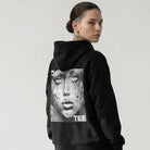 Person wearing a black JAYTEE hoodie with a graphic design on the back, standing against a white background