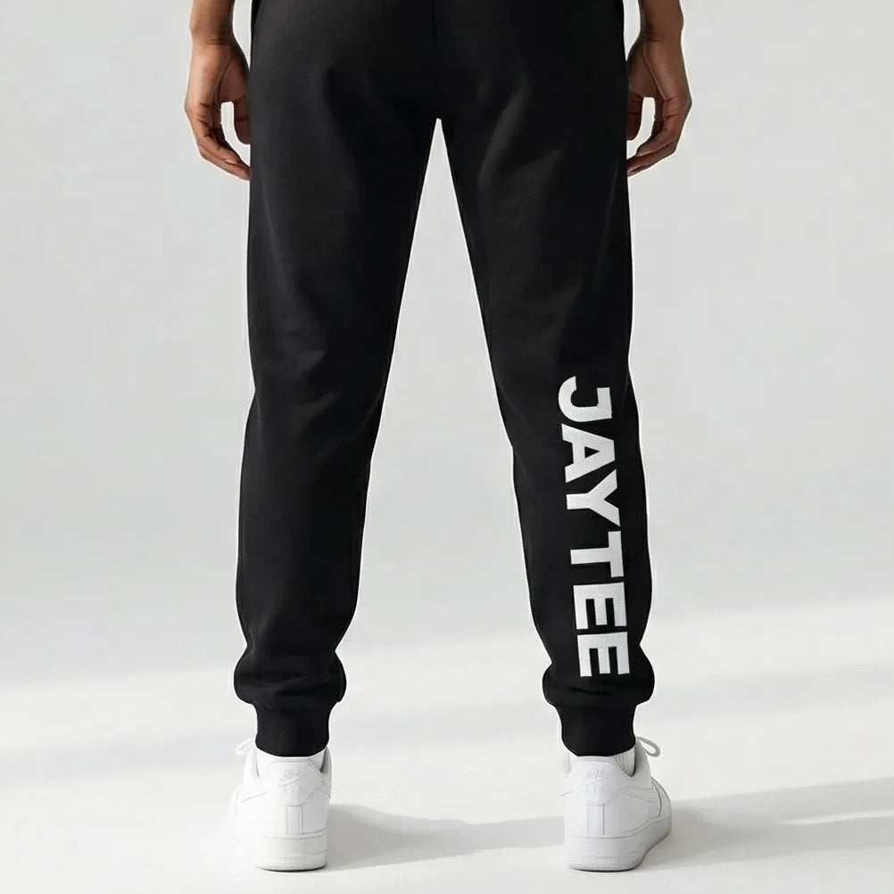 Person wearing a black JAYTEE tracksuit on a white background