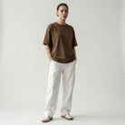 Person wearing a toffee JAYTEE t-shirt and white pants on a plain background