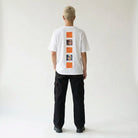 Person wearing a white JAYTEE t-shirt with graphic designs on the back against a plain background