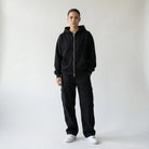 Person wearing a black JAYTEE hoodie and pants with white sneakers on a light gray background