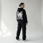 Person wearing a black JAYTEE hoodie with a graphic design on the back against a plain background