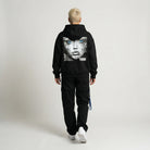 Person wearing a black hoodie with a graphic design on the back against a plain background