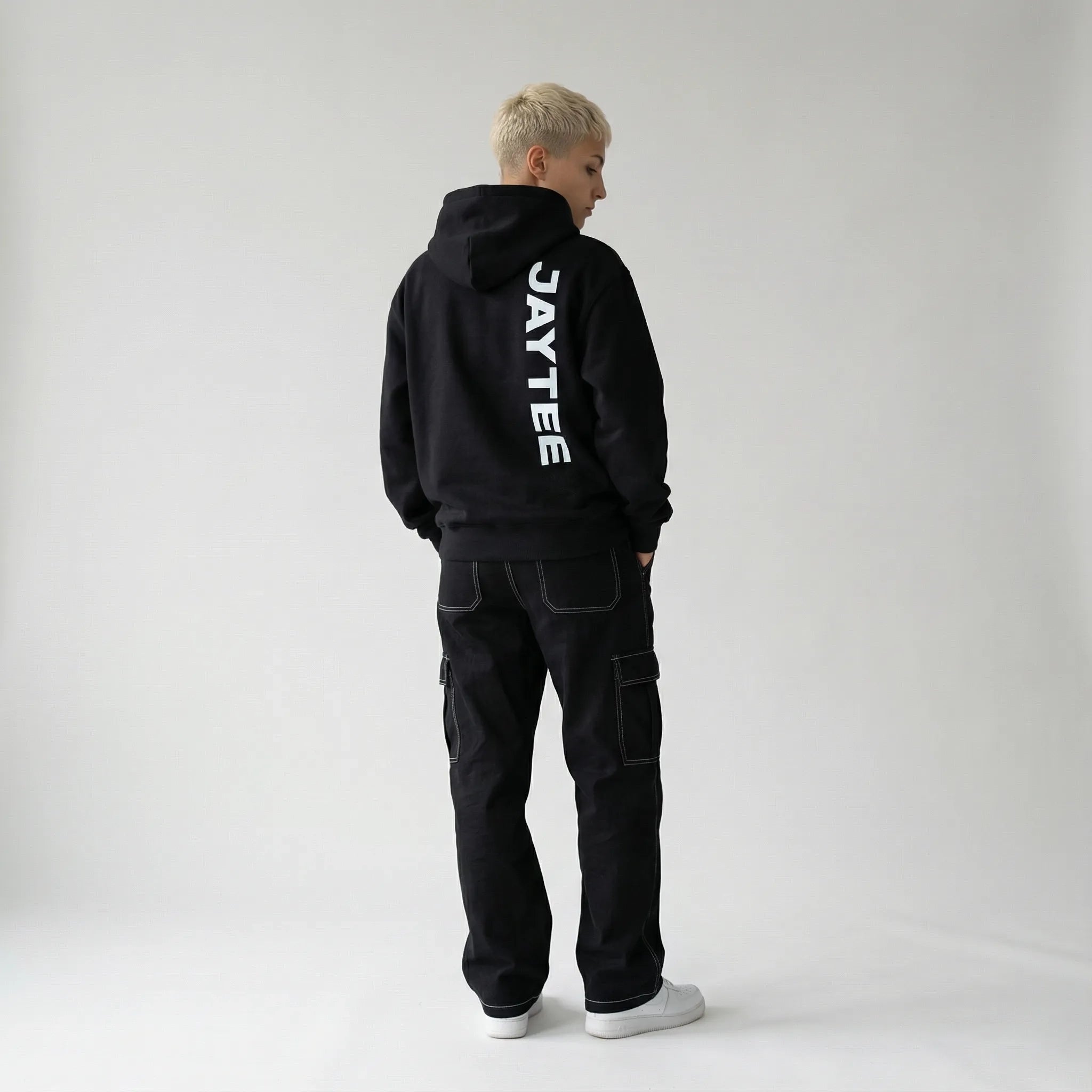 Person wearing a black JAYTEE hoodie with 'JAYTEE' branding on the back, standing against a plain white background.