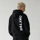 Person wearing a black JAYTEE hoodie with 'JAYTEE' branding on the back, standing against a plain white background.