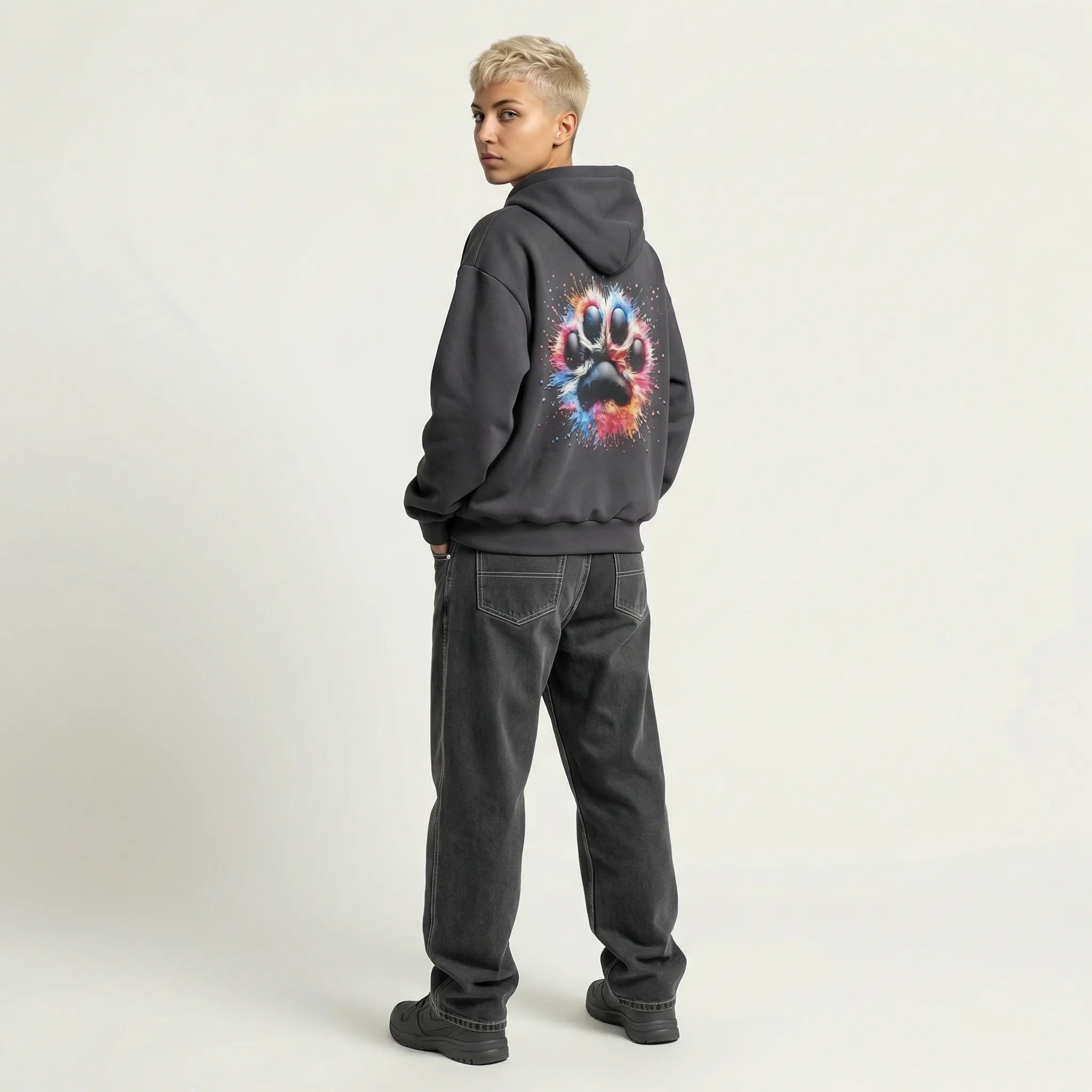 Person wearing a dark hoodie with a colorful paw print design on the back, standing against a plain background.