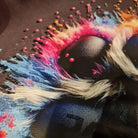 Close-up of a colorful abstract painting with vibrant splashes of pink, blue, and orange on a dark background.