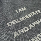Text on a textured surface reading 'I AM DELIBERATE AND AFRAID OF NOTHING', with a focus on the word 'DELIBERATE'.