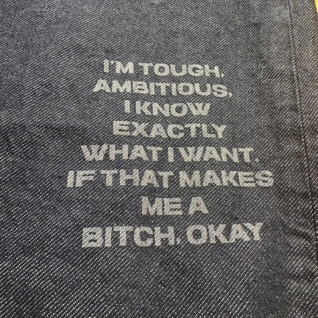 Text on denim fabric stating 'I'm tough, ambitious. I know exactly what I want. If that makes me a bitch, okay.'